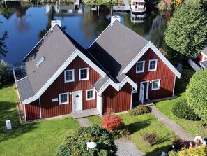 A red two-story house with a sloped roof, a front porch, and a small garden with a pathway leading to the entrance.