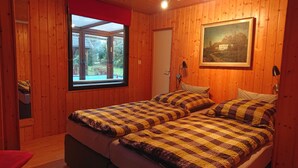 Una habitación de madera con dos camas, una ventana, una puerta y un cuadro en la pared.