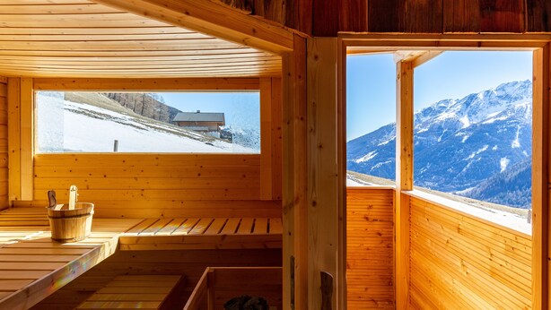Un sauna en bois offrant une vue sur une montagne enneigée et une maison.
