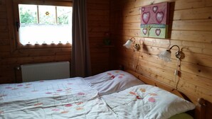 Une pièce de cabane en bois comprenant un lit, un radiateur, une fenêtre avec des rideaux et un tableau mural.