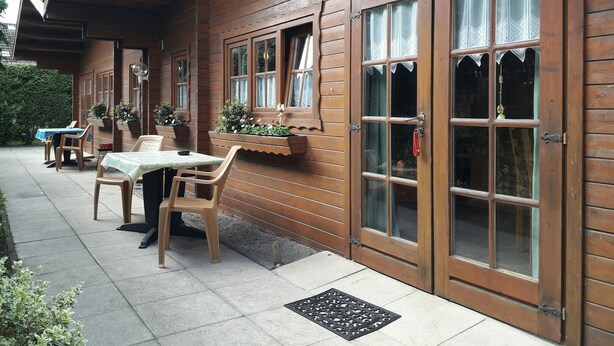 Un bâtiment en bois doté de grandes fenêtres et d’un patio couvert avec des sièges pour l’extérieur.