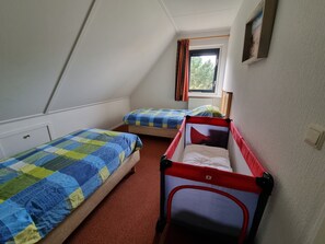 A room with two beds, a red and blue crib, and a window with curtains.
