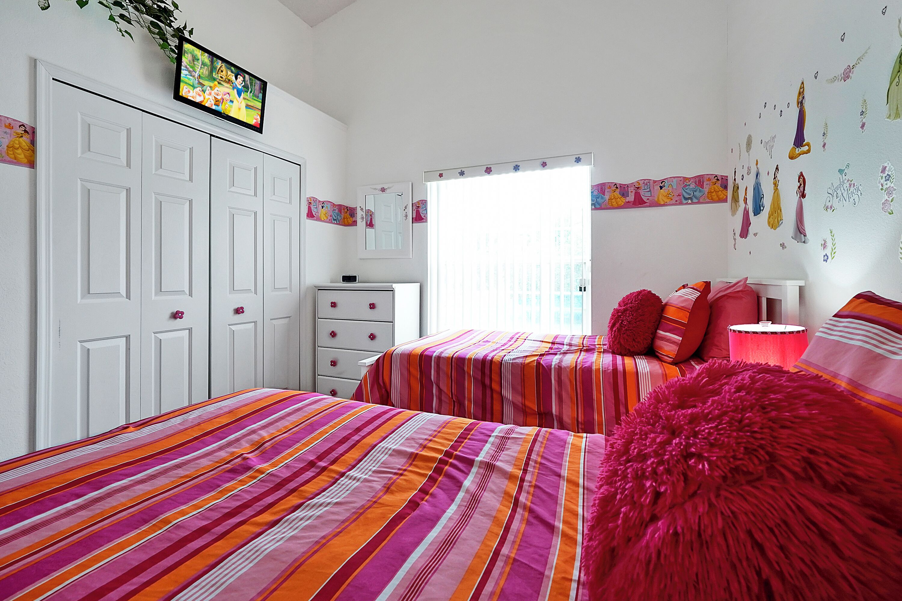 Une chambre avec deux lits, une télévision, une armoire et une fenêtre avec des rideaux.
