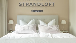 Een netjes opgemaakt bed met witte lakens en kussens, een hoofdbord met een gestuikt ontwerp en twee bedlampen aan weerszijden.