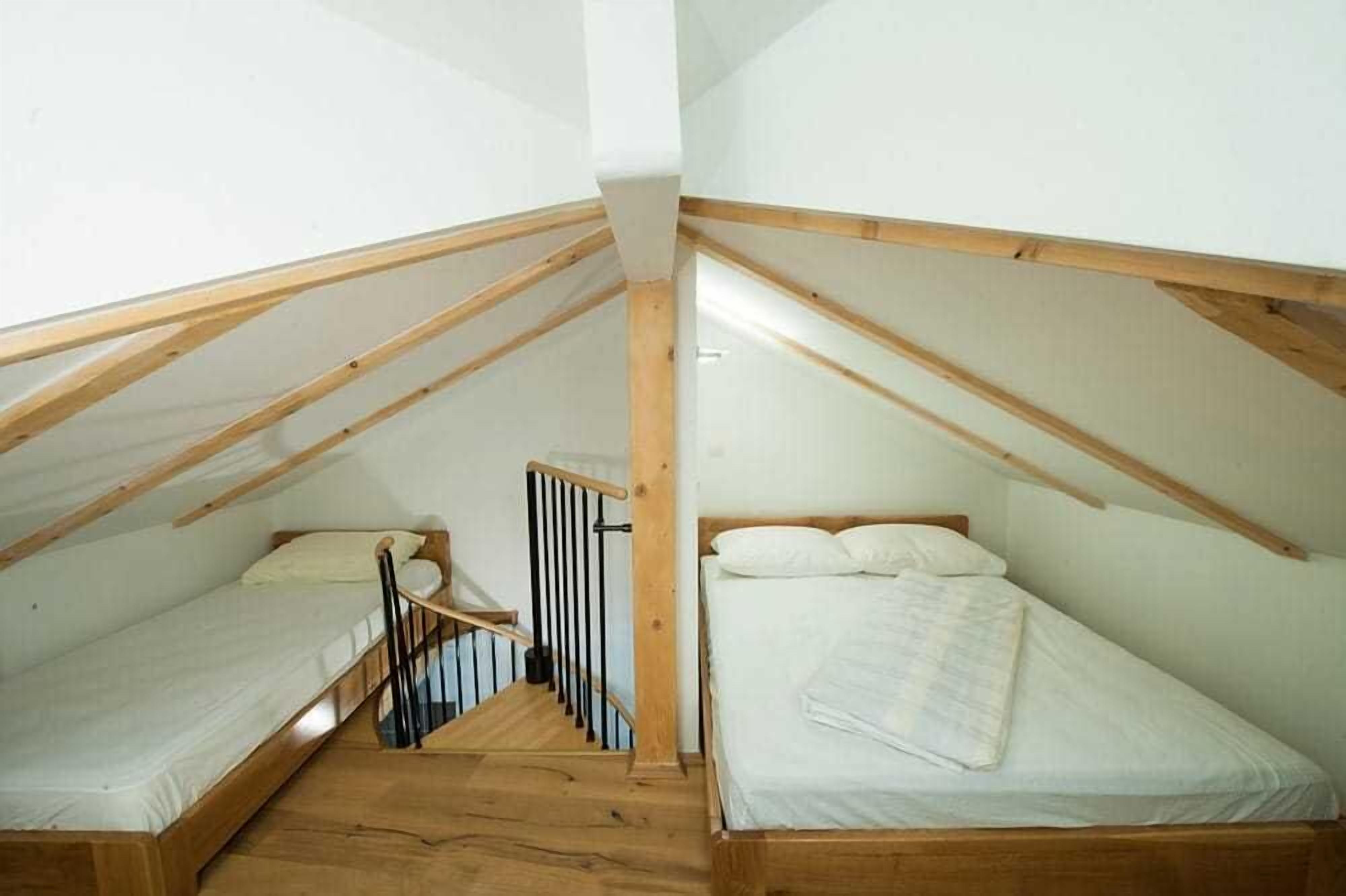 A small attic bedroom with two wooden bunk beds and a wooden staircase.
