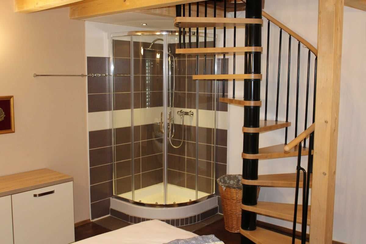 Een douchekamer met een glazen cabine, een houten trap en een betegelde muur.