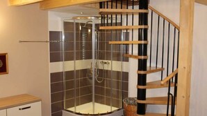 Ein Duschraum mit Glasabtrennung, einer Holztreppe und einer gefliesten Wand.