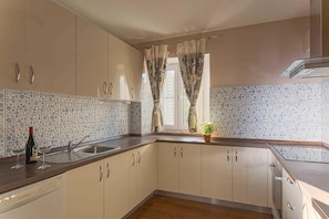 Una cocina con gabinetes color beige, salpicadero de azulejos, un lavamanos y un lavavajillas.