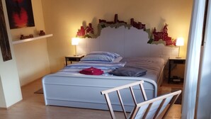 Ein Schlafzimmer mit einem Bett, Nachttischen, einer Wanddekoration mit Stadtansicht, einer Topfpflanze und einem Bild an der Wand.