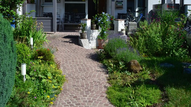 Ein Haus mit einem Ziegeldach, einer Veranda und einem Gartenweg, der zum Eingang führt.