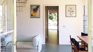 Een ruime woonkamer met een trap, een eettafel met stoelen, en kunstwerken aan de muur.