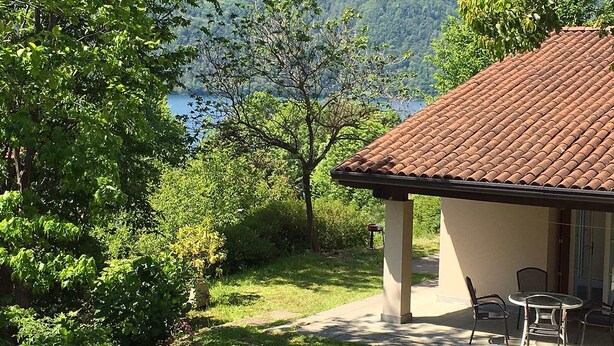 Een huis met een pannendak, een terras met stoelen en uitzicht op een meer en bergen.