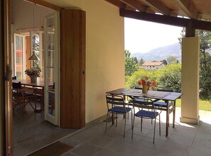 An open patio with a table and chairs, a wooden door, and a view of a mountain and greenery.