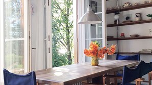 Een eetgedeelte met een houten tafel en blauwe stoelen, een vaas met bloemen, en een boekenkast met boeken en decoratieve objecten.