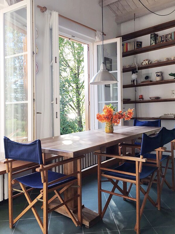 A dining area with a wooden table and blue chairs, a vase with flowers, and a bookshelf with books and decorative items.