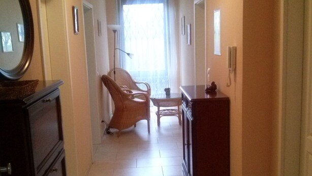 Ein Korridor mit einem Holzkasten, Korbstühlen, einem kleinen Tisch und einem Schrank.