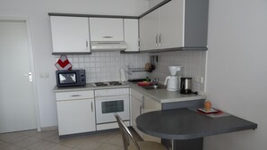 A compact kitchen with white cabinets, a microwave, a stove, a coffee maker, and a small dining table with two chairs.