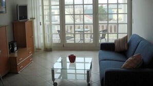 A living room with a sofa, a glass coffee table, a TV on a cabinet, and a view of the outside balcony.