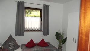 Une chambre à coucher avec un lit, une fenêtre avec des rideaux, une lampe de chevet et une plante en pot.