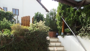 Un espace patio avec une table ronde et deux chaises, un petit escalier et un pot de fleurs orné de fleurs rouges.
