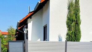 Une maison moderne avec une façade blanche, un toit rouge et une clôture en métal grise.