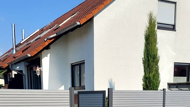 Un bâtiment moderne doté d’un toit en pente, d’une entrée fermée par un portail et d’une petite fenêtre.