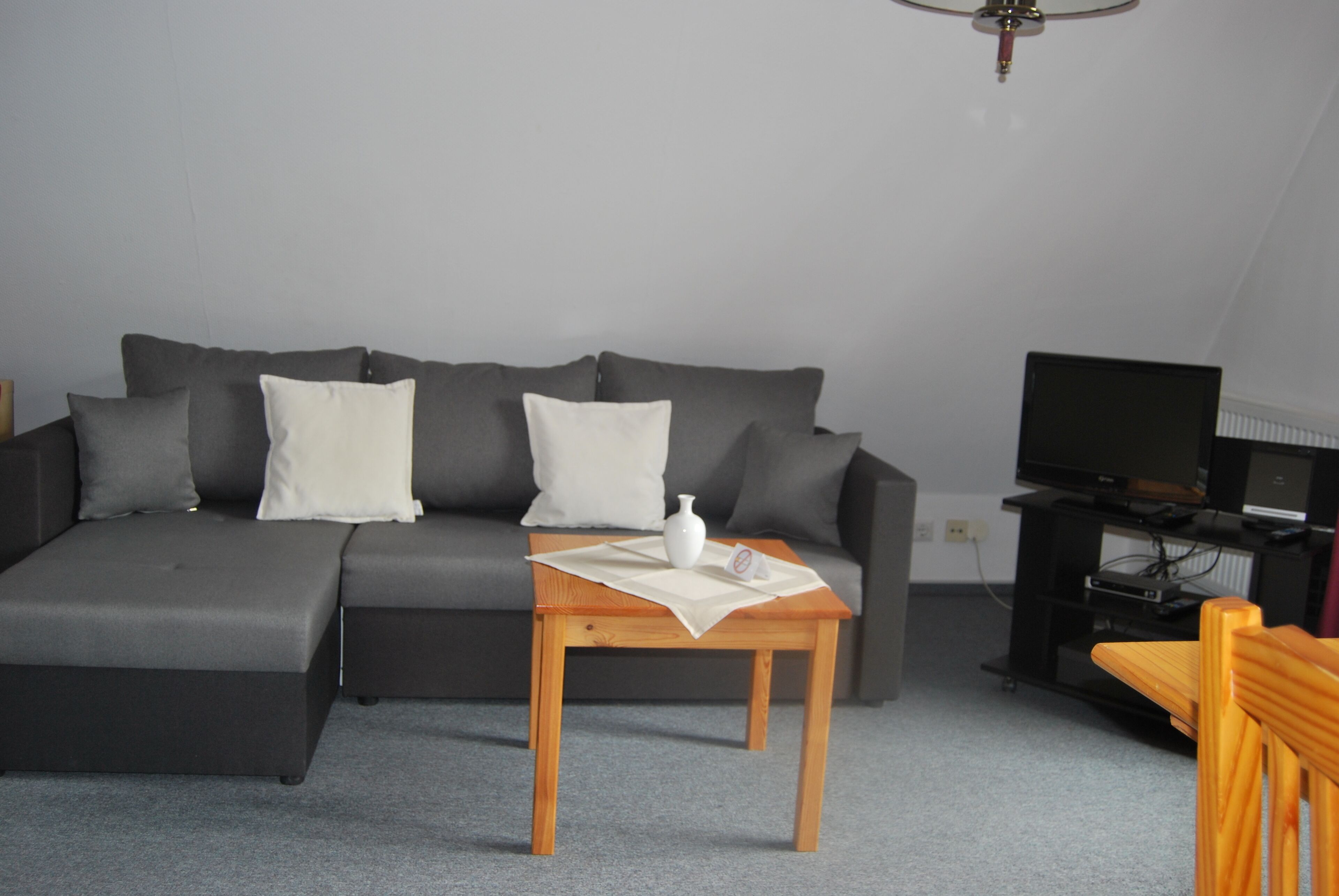 Ein modernes Wohnzimmer mit einer grauen Eckcouch, einem Holztisch und einem Fernseher auf einem Lowboard.