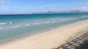 Une plage à l’eau turquoise et limpide, un rivage sablonneux et, au loin, des montagnes sous un ciel bleu.