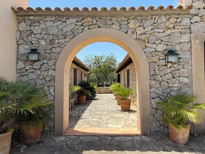 Un arco de piedra que da acceso a un patio con plantas en macetas y suelo de baldosas.