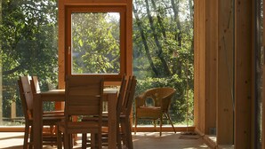 Un coin repas en bois, avec une table et des chaises, de grandes fenêtres et une vue sur les arbres.