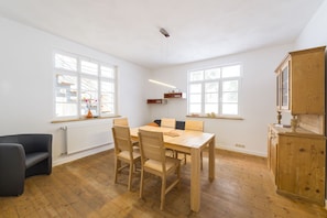 A spacious room with a wooden dining table, chairs, a black sofa, and a wooden cabinet.