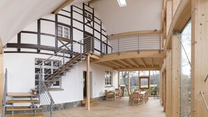 Un intérieur spacieux avec un escalier en bois, un coin repas et de grandes fenêtres offrant une vue sur l’extérieur.