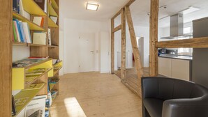 Une pièce avec une bibliothèque en bois, un fauteuil en cuir noir et un coin cuisine avec une fenêtre.