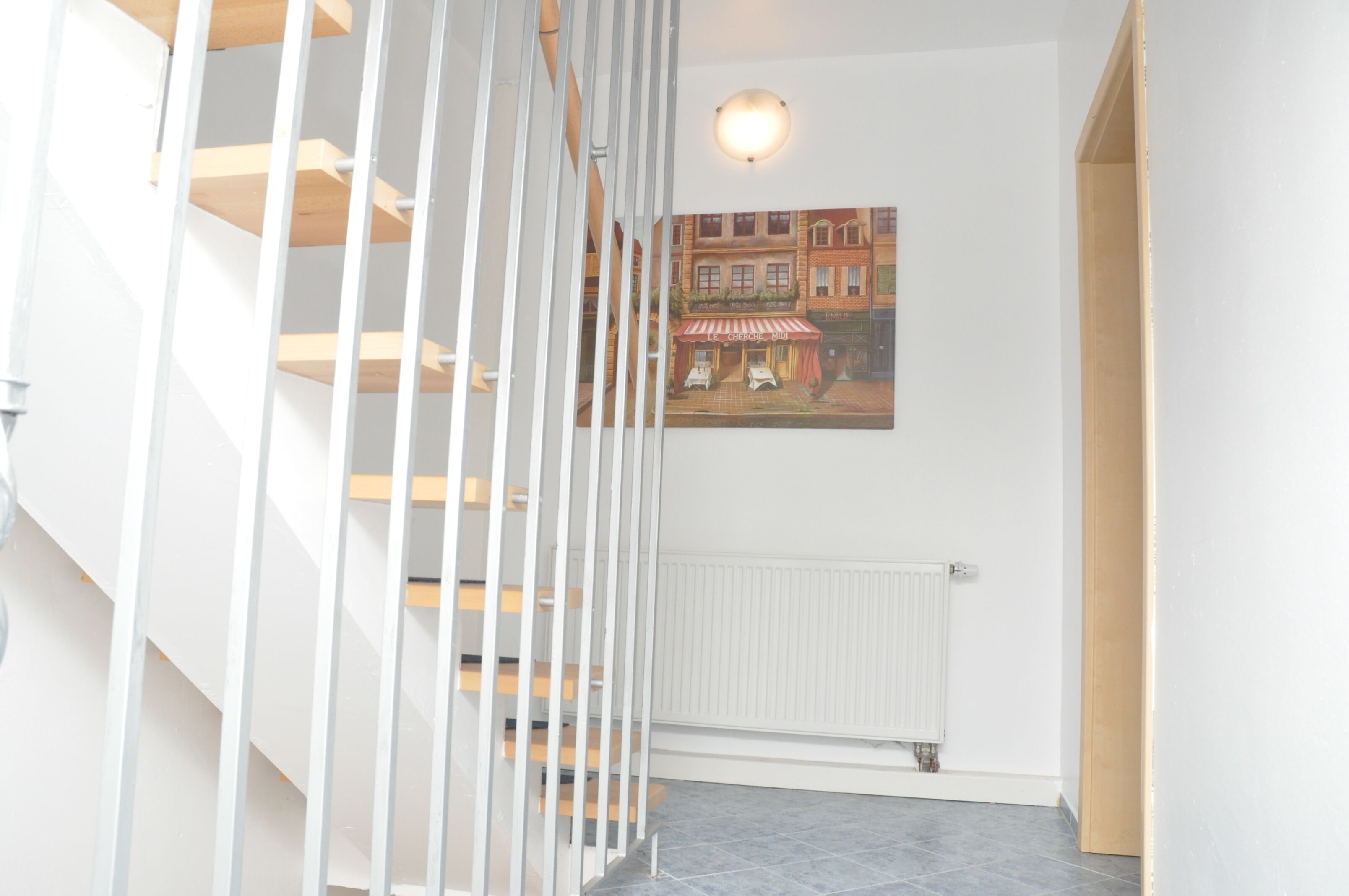 A staircase with white railings and wooden steps, a white radiator, and a framed picture of a street scene on the wall.