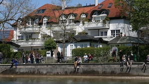 Un grand bâtiment blanc, doté d’un toit recouvert de tuiles rouges et de nombreuses fenêtres, situé au bord d’une étendue d’eau.