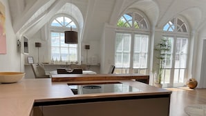 Une cuisine moderne dotée d’un îlot central, de meubles blancs et de grandes fenêtres.