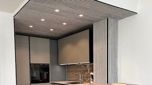 Une cuisine moderne avec un îlot central en bois, des meubles gris et un plafond en pente doté d’un éclairage encastré.