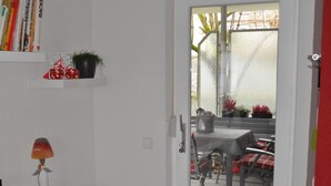 Een kamer met een witte deur die leidt naar een terras buiten, met een tafel en stoelen.