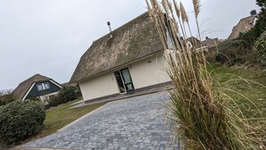 A house with a thatched roof, a paved driveway, and a well-maintained lawn. - Top Vacation Villa, 120 sqm, Near the Beach, Quiet, 3 Bedrooms, 2 Bathrooms, Fireplace, Wi-Fi (Julianadorp aan Zee)