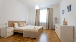 Een moderne slaapkamer met een houten vloer, een bed met een beige dekbedovertrek, een nachtkastje met een lamp en een dressoir.