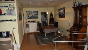 A spacious room with a dining table, chairs, a guitar, shelves with collectibles, and artwork on the walls.