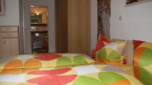 A bedroom with a bed featuring a multicolored circular pattern bedspread, a wooden headboard, and a wall-mounted painting.