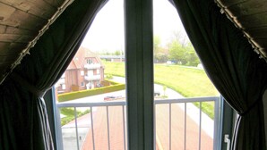 Vista desde una ventana con cortinas, que da a una calle residencial con casas y un área verde.