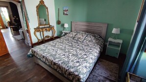 Une chambre à coucher comprenant un lit, une table de chevet, une commode, un miroir et une porte donnant sur une autre pièce.