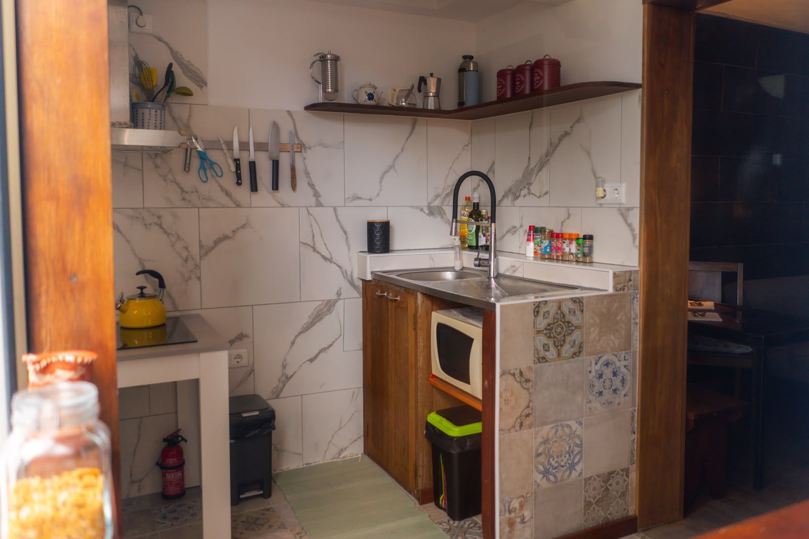 Una cocina compacta con un lavamanos, una tetera amarilla y diversos utensilios de cocina.
