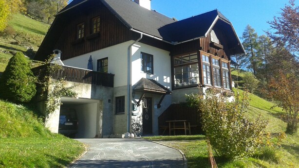 A large, two-story house with a steeply pitched roof, a garage, and a well-maintained lawn.