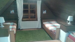 A small, cozy attic bedroom with a sloped ceiling, two single beds, a window with curtains, and a small green rug.