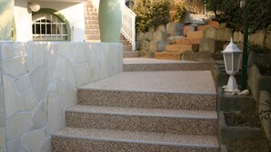 Un escalier en pierre menant à l’entrée d’un bâtiment, avec un mur de pierre d’un côté et une lanterne de l’autre.