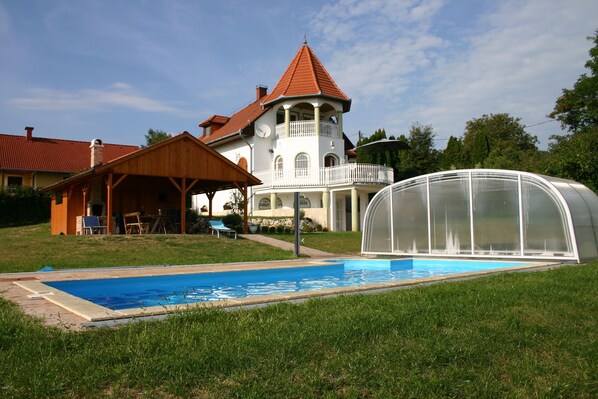 Une grande maison avec une piscine, une serre couverte et un kiosque en bois.