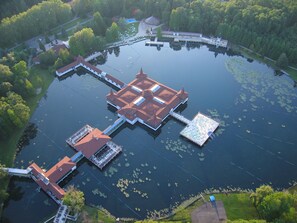 Une vue aérienne d’une vaste étendue d’eau circulaire, avec une île centrale sur laquelle se trouve un bâtiment traditionnel doté d’un toit rouge et de plusieurs annexes.